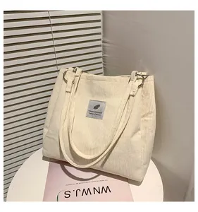 Detail of off-white corduroy tote bag showing ribbed texture and square logo label