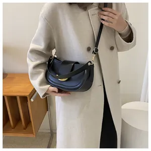 Detail of a black leather saddle bag with gold buckle worn on a beige wool coat