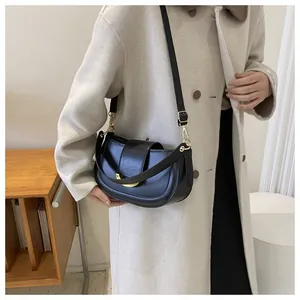 Black saddle bag with glossy finish and gold hardware shown on a beige coat outfit