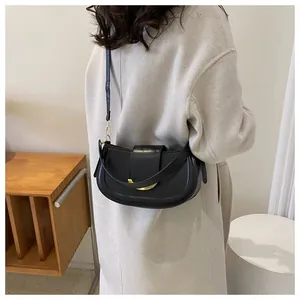 Minimalist black matte saddle bag with gold metal hardware worn over an ivory winter coat