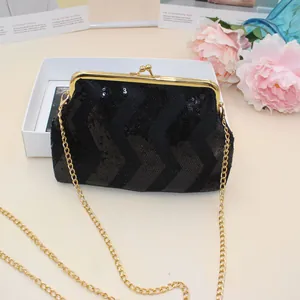 Detail of black sequin evening bag with gold metal clasp and chain strap on light surface