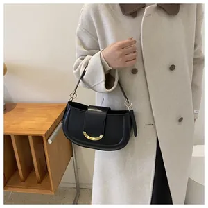 Detail of minimalist black saddle bag with gold metal buckle on a beige wool coat