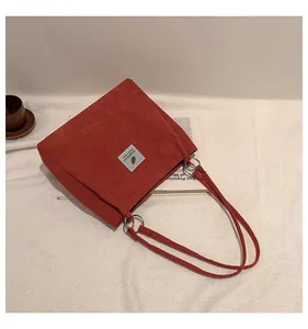 Detail of red-brown corduroy tote bag featuring a gray fabric label and metal ring buckles