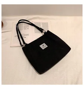 Detail of black corduroy tote bag showing textured fabric, leaf patch and metal ring
