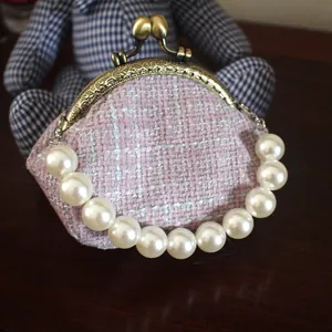 Detail van roze tweed clip portemonnee met parelhandvat en vintage goudkleurig metalen frame