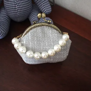 Detailopname van grijze tweed portemonnee met vintage sluiting en parelhandvat