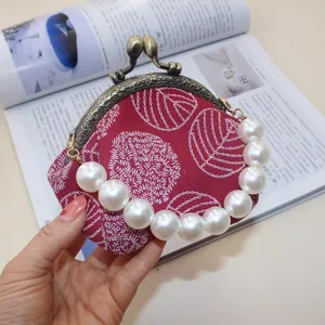 Close-up of canvas clasp purse with leaf embroidery and white pearl handle strap