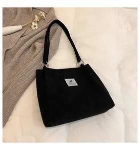 Detail of black corduroy tote bag with silver metal rings and white woven label