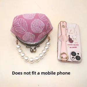 Pink embroidered clasp purse with pearl handle shown next to phone to illustrate small size