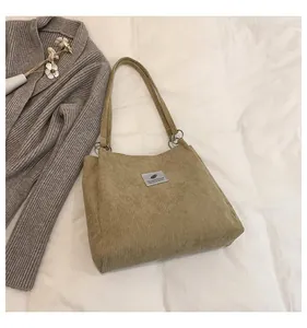 Detail of corduroy tote bag texture showing grey fabric label and silver metal ring strap