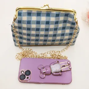 Detail van geruite stoffen minitas met gouden sluiting en ketting naast een telefoon
