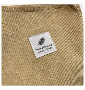 Close-up of khaki corduroy fabric featuring a white patch with black feather and text