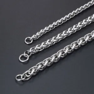 Close-up of three sizes of silver-toned wheat chain necklaces on a dark textured surface