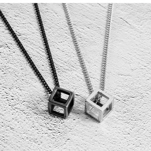 Close-up of minimalist black and silver hollow cube necklaces on textured surface