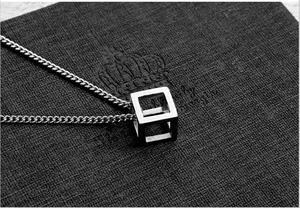 Macro shot of silver hollow cube pendant on link chain against black texture background