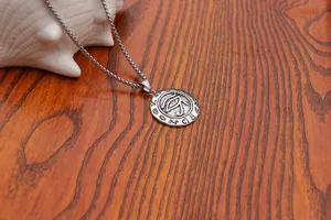 Detailed close-up of Eye of Horus relief pendant on round box chain over a white shell