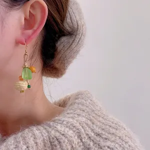 Détail de boucles d'oreilles faites main avec perle tissée et perles vertes sur modèle