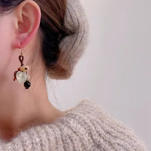 Détail de boucles d'oreilles artisanales avec accents de pomme de pin et feuille sur crochet or