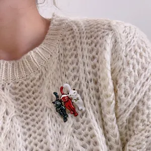Three-piece cat enamel brooch set in black, red, and white on a beige knit sweater