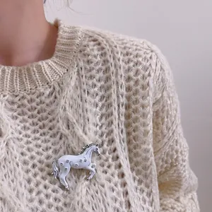Gros plan d'une broche cheval argentée avec cristaux sur un pull en maille blanc