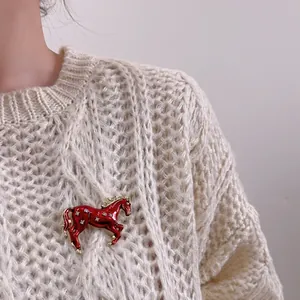 Broche cheval au galop avec émail rouge et cristaux sur un pull en tricot blanc