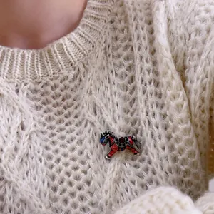 Vintage horse brooch with red enamel and crystals pinned on a beige knitted sweater