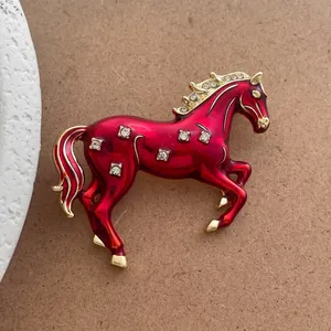 Détail macro d'une broche cheval en émail rouge avec bordure dorée et cristaux incrustés