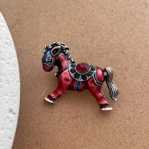 Macro shot of vintage horse brooch with red enamel, crystal saddle, and silver details