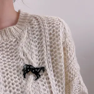 Détail d'une broche de cheval noir émaillé et diamants sur un pull en maille beige