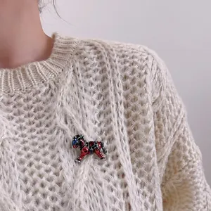 Detail of red enamel galloping horse brooch with diamond accents on a white knit sweater
