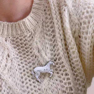 Broche cheval au galop en émail blanc et strass scintillants sur un pull en maille douce