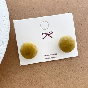Detailed view of mustard green velvet flocked ball stud earrings on white display card
