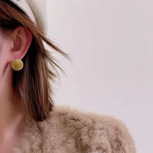 Macro view of mustard yellow flocked ball stud earring worn with a stylish winter outfit
