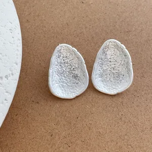 Dettaglio di orecchini a cuore irregolari in argento con texture martellata su legno