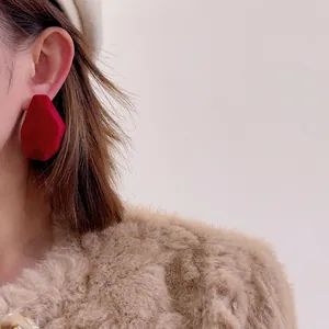 Close-up of burgundy flocked irregular geometric stud earring worn by a model