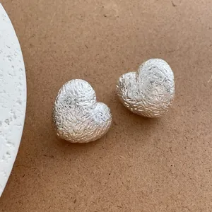 Vista macro di orecchini a cuore argento con texture martellata su sfondo cartaceo