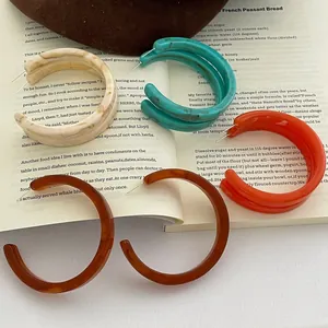 Retro amber brown C-shape acetate hoop earrings displayed on an open vintage book page