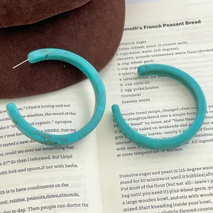 Retro turquoise C-shaped chunky acetate earrings with marble pattern on a book
