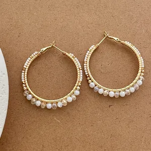 Vintage large gold hoop earrings with handmade white beads and crystals on paper background