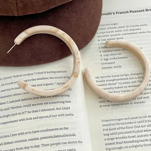 Vintage C-shaped acetate earrings with cream marble texture on a brown wool hat and book