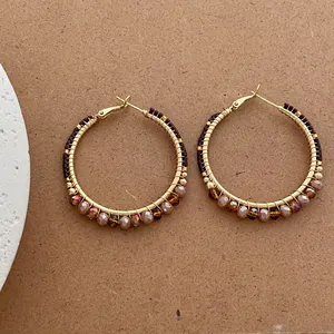 Macro view of bohemian gold wire hoop earrings with brown beads on textured background