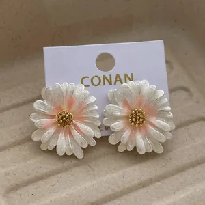 Elegante weiße Gänseblümchen Ohrstecker mit goldener Mitte und Glitzer auf beigem Tablett