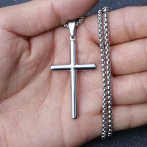 Polished stainless steel cross pendant on box chain held in palm for size reference