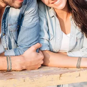 Detail of silver Cuban link chain bracelets worn by a couple in an outdoor setting