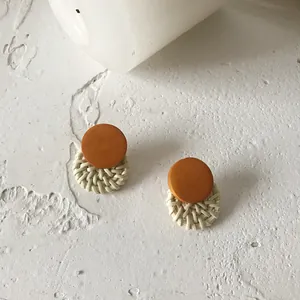 Retro bohemian round woven rattan earrings with orange wood studs on stone surface