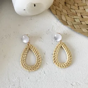 Detail of bohemian waterdrop straw woven earrings with clear acrylic studs on white texture