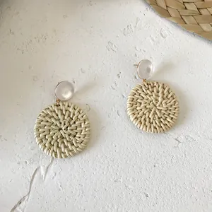 Detail of round straw woven drop earrings with white resin stud for summer beach style