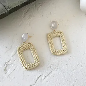 Close-up of bohemian earrings with white resin studs and woven straw drop charms
