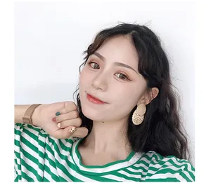 Close-up of retro rattan woven earrings with cream-colored disc on a model with striped shirt