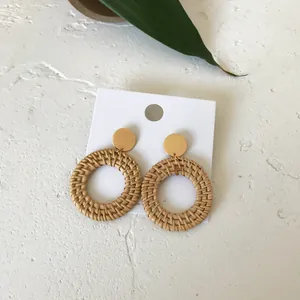 Close-up of handmade round rattan drop earrings with gold studs on a display card
